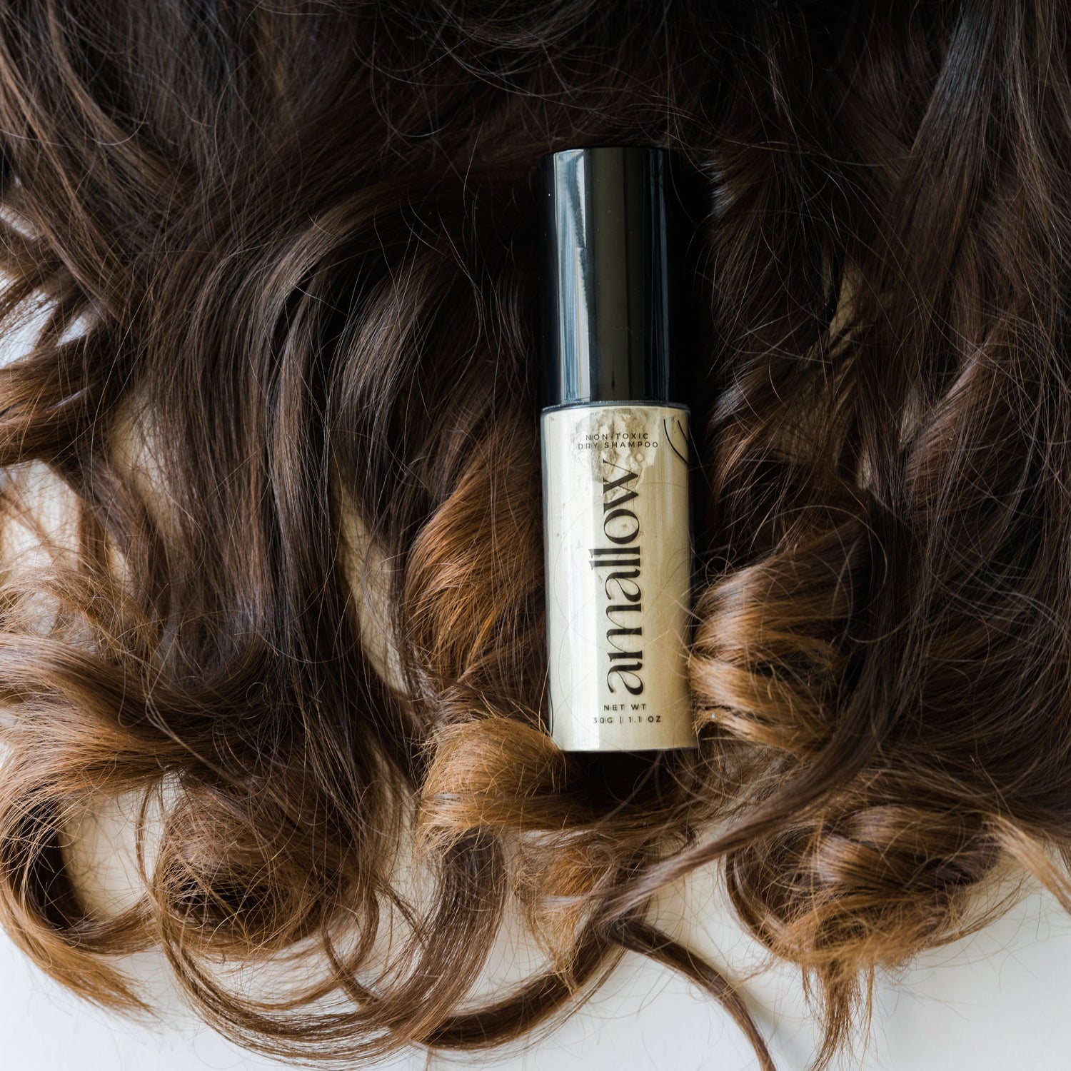 Picture of the container of dry shampoo laid on someone's hair.