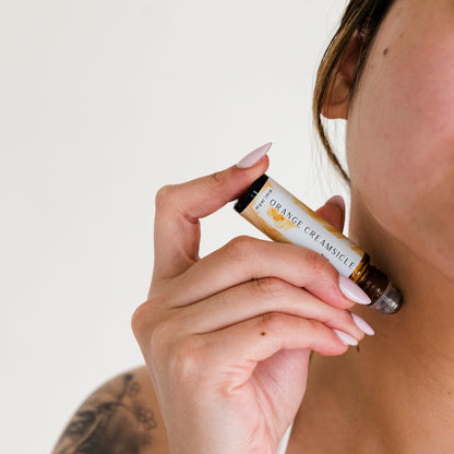 Woman applying orange creamsicle perfume roller to her neck